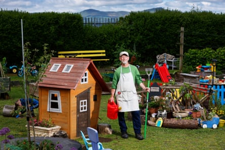 Phil Morris stands in a playground while holding gardening tools