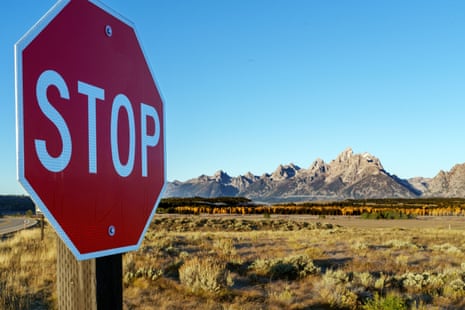 A stop sign stands before grassland, with Grand Teton national park's jagged mountains beyond
