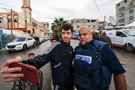An Arab man in a bullet-proof vest marked ‘press’ poses for a selfie with a young man in a street