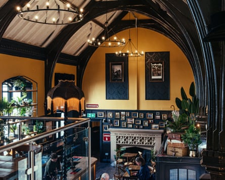 A pub interior with high arched ceilings, yellow painted walls, a fireplace and a fringed lamp.