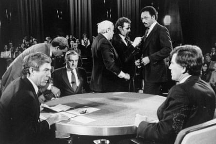 White and Black men, but mostly white men, sit and stand around a round table.