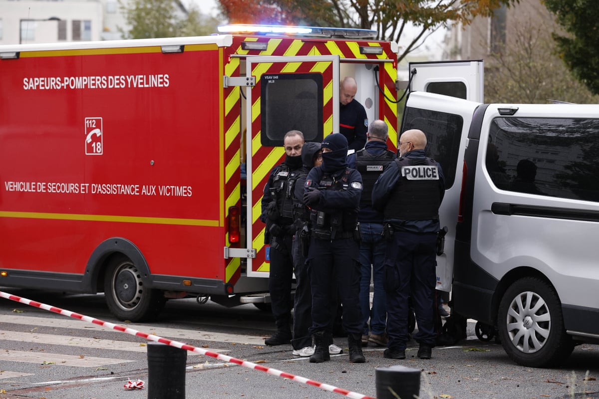 Police officers gather by a fire service vehicle and mortuary van in Trappes, France