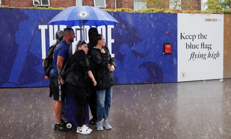Fans shelter themselves from the rain outside the stadium prior to the Premier League match between Chelsea and Luton Town at Stamford Bridge.