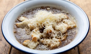 A white bowl of French onion soup with grated cheese on top