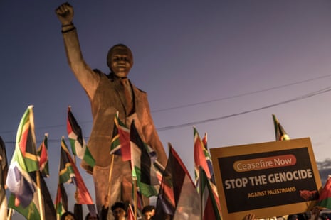 People raise flags and placards as they gather around a statue of late South African president Nelson Mandela in Ramallah