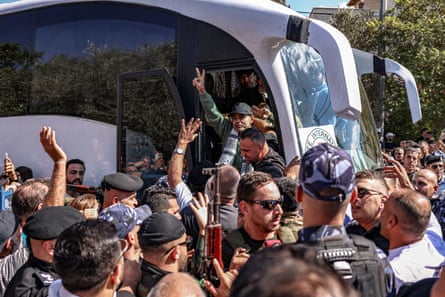 Crowd gathers at the door of the bus as men depart it, one holding up his fingers in a ‘V’ sign
