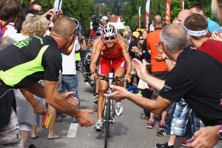 A woman finishing a cycling road race with people either side cheering her on and a camera person filming behind