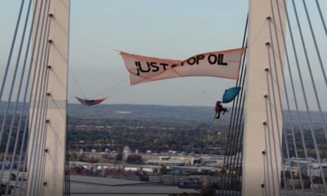 A 'Just Stop Oil' banner displayed on the bridge, with the two men suspended on ropes.