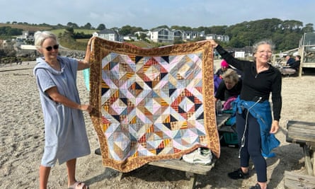 Two swimmers hold up gifted quilts on Swanpool beach.
