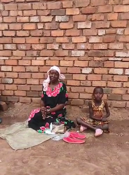 Babirye Zainab and her grandmother sitting on the ground in front of a brick wall