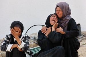 Three weeping women comfort one another with rubble in the background