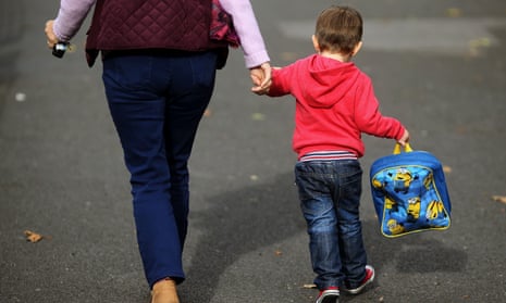 An adult is holding a young child's hand, who is carrying a schoolbag