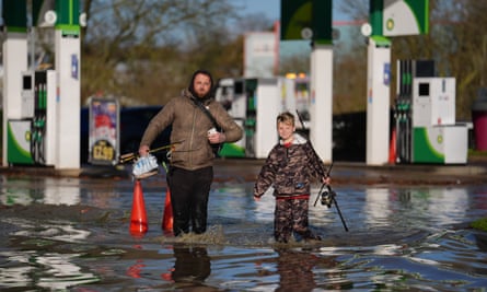 A man and a boy with fishing gear wading through water at a petrol station.