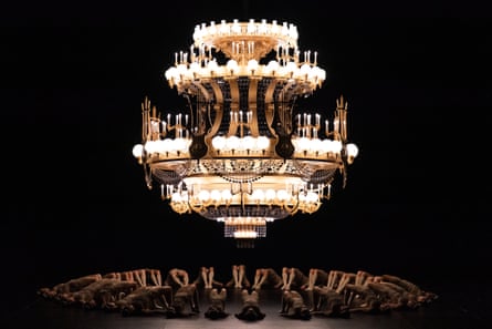 Ballet dancers form a circle underneath a huge chandelier