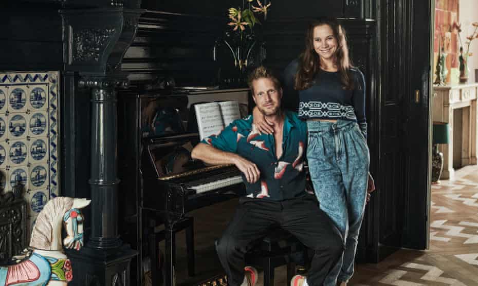 Elmar Krop with his partner, Claudia Smithson, next to their piano in a dark wood panelled room