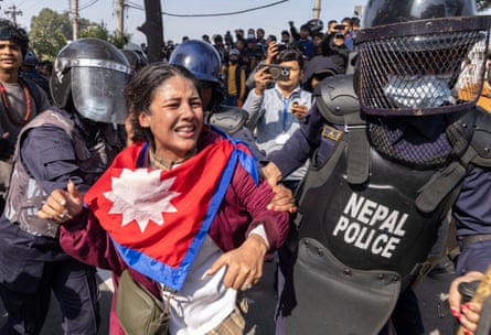 A toung woman in traditional clothes is held by the arms by riot police.