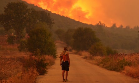 A man standing on a path that leads to a huge wildfire