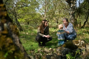 The Princess of Wales in a forest on the Isle of Mull bends down to speak to a child and an adult.