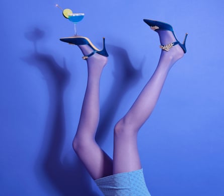 Woman from thighs down, with legs in the air, in high heels, with a cocktail glass balanced on the sole of her left foot