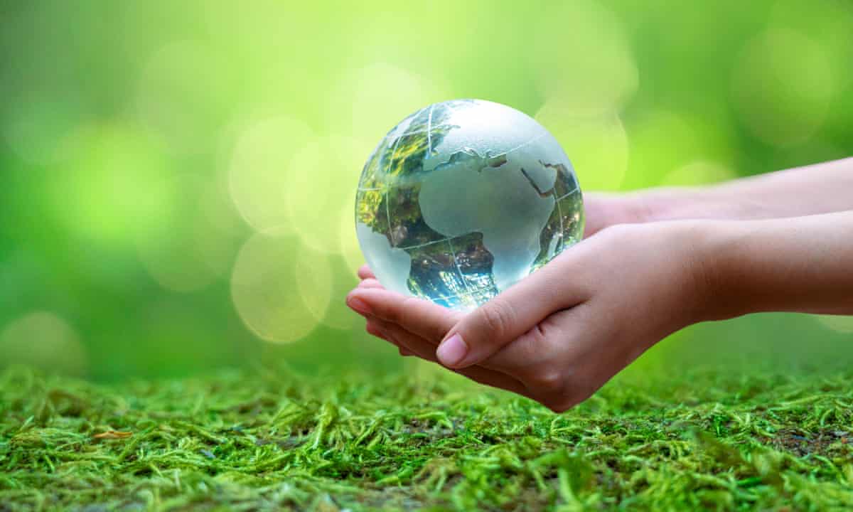 A glass earth held by human hands over a mossy ground