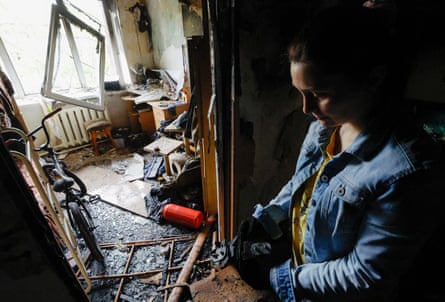 A woman stands among fallen and damaged items including a blown-out window