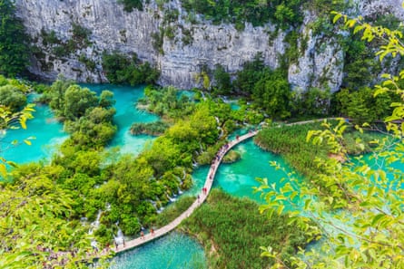 People walking on a wooden walkway over turquoise lakes with a cliff in the background