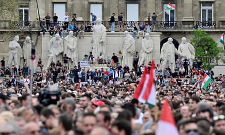 A large crowd of people with banners and Hungarian flags, some of them sitting and standing on the Kossuth Memorial