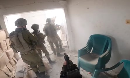 A image of four Israeli soldiers standing with their backs to the camera in the entrance of a damaged building 