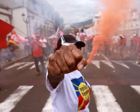 A man holds his fist towards the camera, with other marchers holding flares and flags in the background