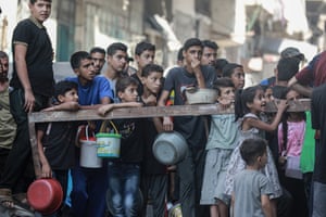 Adults and children queue holding buckets and basins