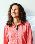 A woman with shoulder length frizzy hair and patterned shirt smiles as she looks away from the camera.