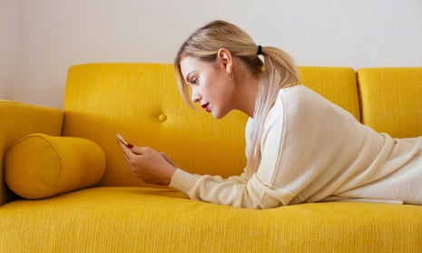 Blonde woman lying on sofa, using smartphone at home