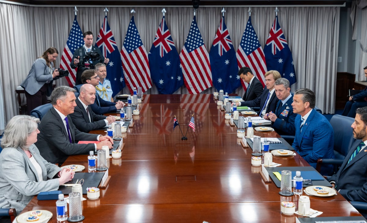 People at a meeting table in front of US and Australian flags