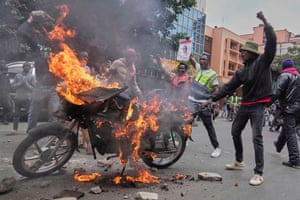 Bike on fire with people with raised fists nearby
