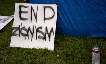 A white square with black lettering dripping down says End Zionism, in green grass leaning against a blue tent.