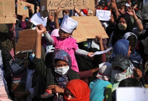 A woman carries a child as refugees and migrants protest after the news about the creation of a new temporary camp.