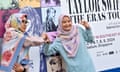 Two women wearing colourful headscarves pose in front of a Taylor Swift Eras Tour billboard advertising concerts in Singapore.