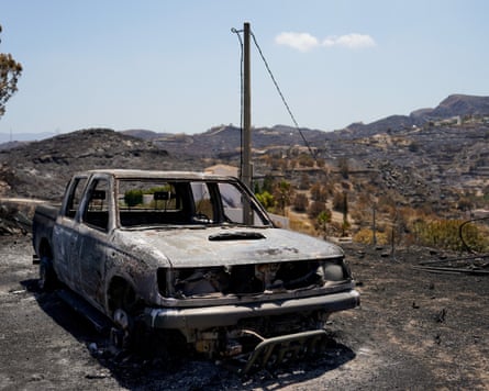 A burnt-out car in against a charred hillside