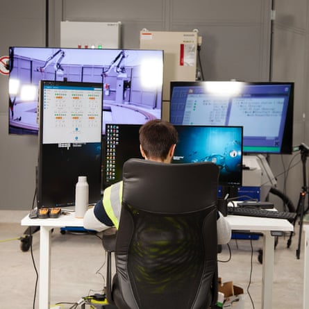 A man sits with his back to the camera working at a bank of computers