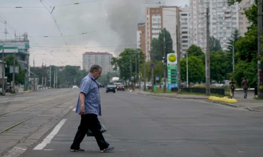 A man crosses a street as smoke rises in the background after Russian missile strikes in Kyiv.