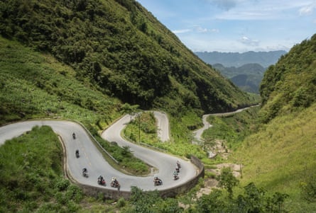 Nine motorbikes, all with passengers riding pillion, on a winding mountain road in Vietnam