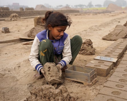 A young girl puts clay into a brick mold