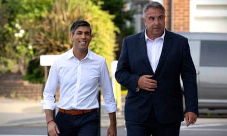 Rishi Sunak, in a shirt and with a bracelet on his right wrist, grins while walking next to Steve Tuckwell, his hand on his jacket