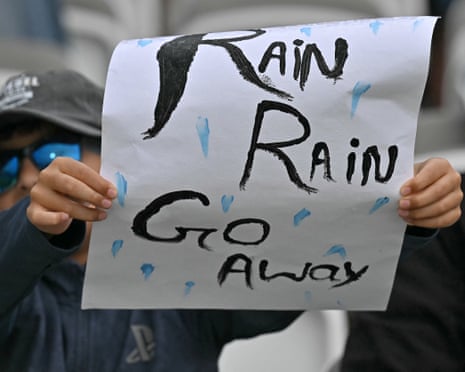 Um torcedor segura uma placa que diz 'Rain Rain Go Away' enquanto os atrasos da chuva tocam novamente.