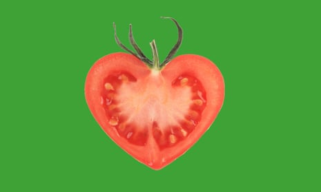 A heart-shaped tomato, sliced in half, on a green background