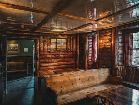 A snug bar lined with wooden logs and filled with wooden benches, tables and chairs