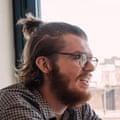 Headshot of a bearded man in a checked shirt, hair pulled up, side on