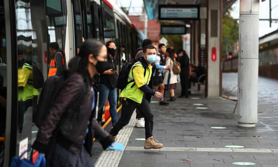 Commuters wearing masks disembark from the light rail at Central station in Sydney, Australia