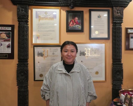 A younger woman smiles in front of a wall with certificates and pictures hung on it.