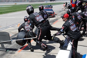 Pit crew in black overalls prepare a tyre change as a car approaches